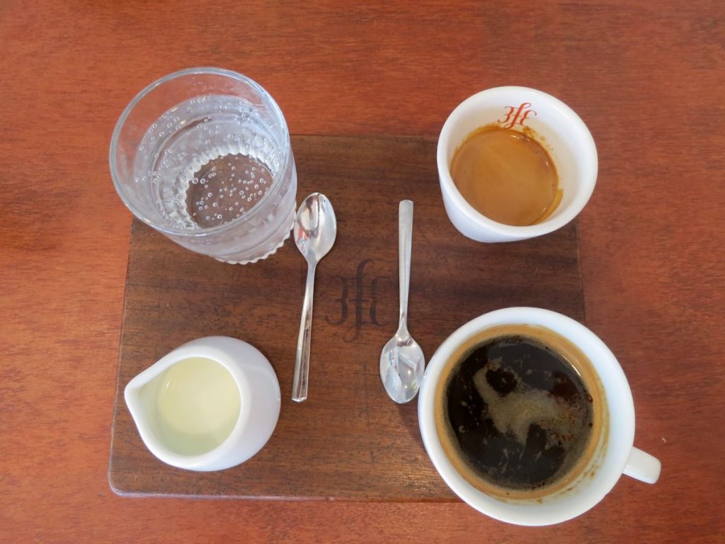 wooden tray with a cup of coffee, milk, espresso and water.