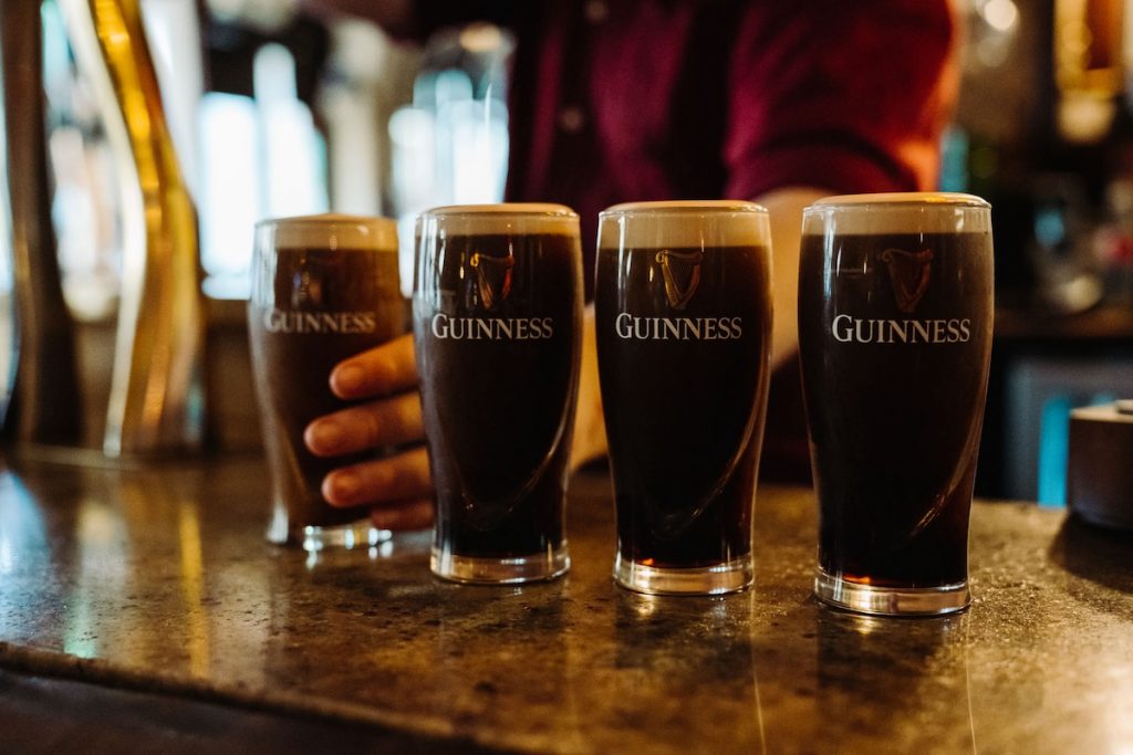 A bartender pours pints of Guinness at a Dublin pub. A row of four pints of Guinness are in a row on the counter.