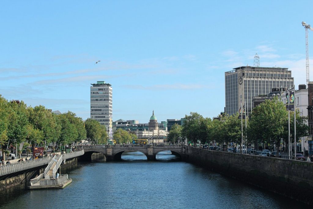 A stone bridge crosses the River Liffey in Dublin, with the Custom House’s green dome and tall city buildings in view.