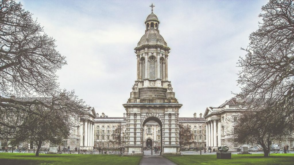 A tall stone bell tower rises over a university courtyard in winter, surrounded by neoclassical buildings and bare trees beneath cloudy skies.