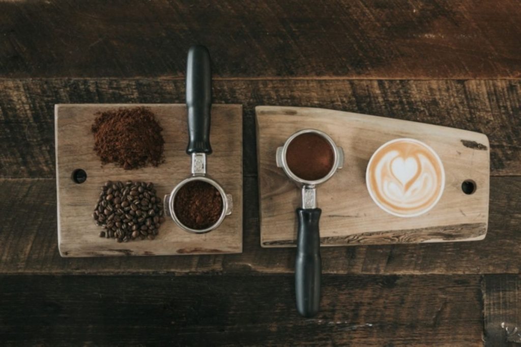 wooden trays with coffee beans, portafilters, and cup of coffee.