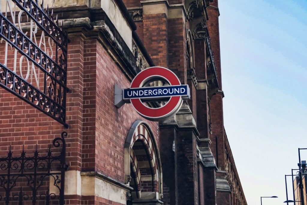 A red and blue London Underground sign hangs outside of a station. 