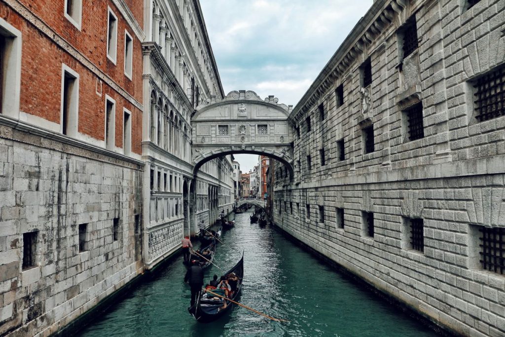 gondolas in the water floating under a bridge that connects two buildings