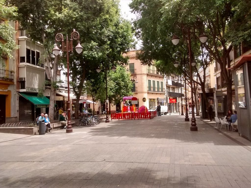 a square in seville filled with trees and some people dining