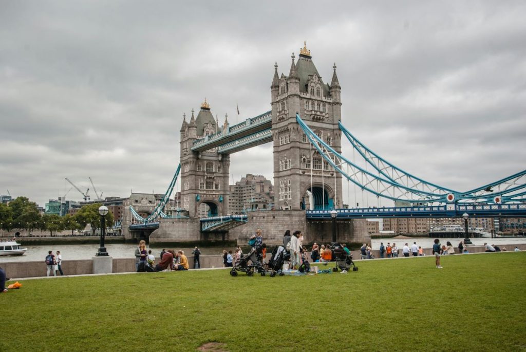 People sitting in front of the Tower bridge in London.