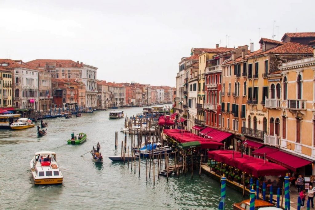 Different types of boats in a large canal with buildings on either side