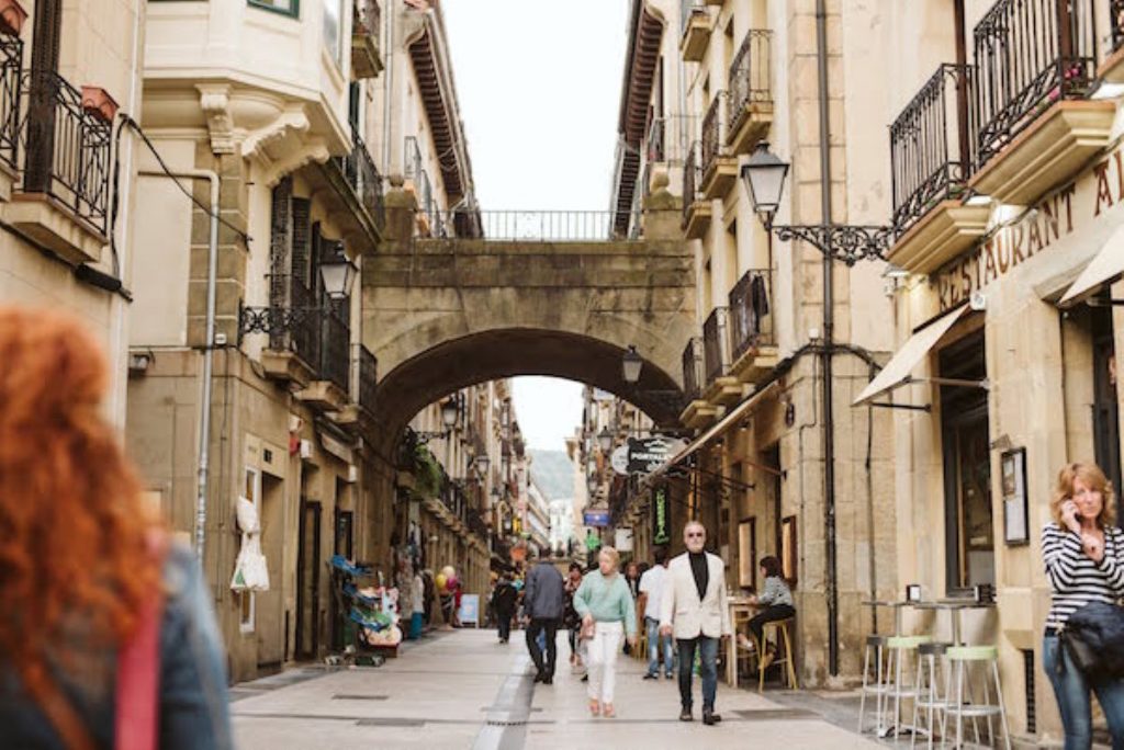 image of people walking down street with buildings joined by arched walkway