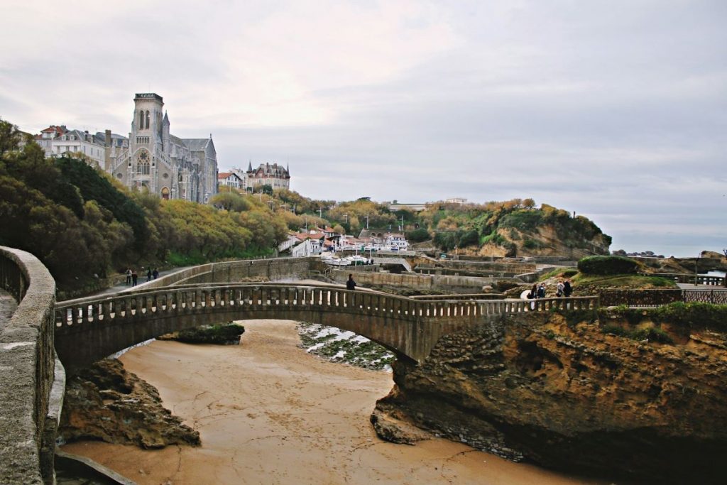 People walking over a bridge going over the beach in Biarritz.  