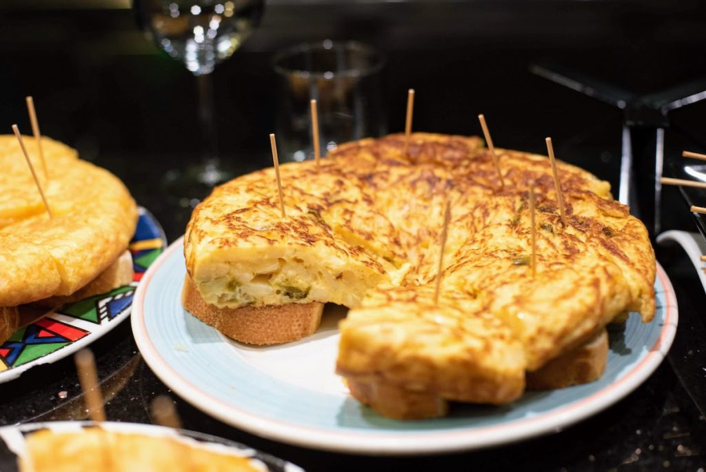 A sliced Spanish tortilla rests on bread, each piece secured with a toothpick, resembling San Sebastian Old Town pintxos.