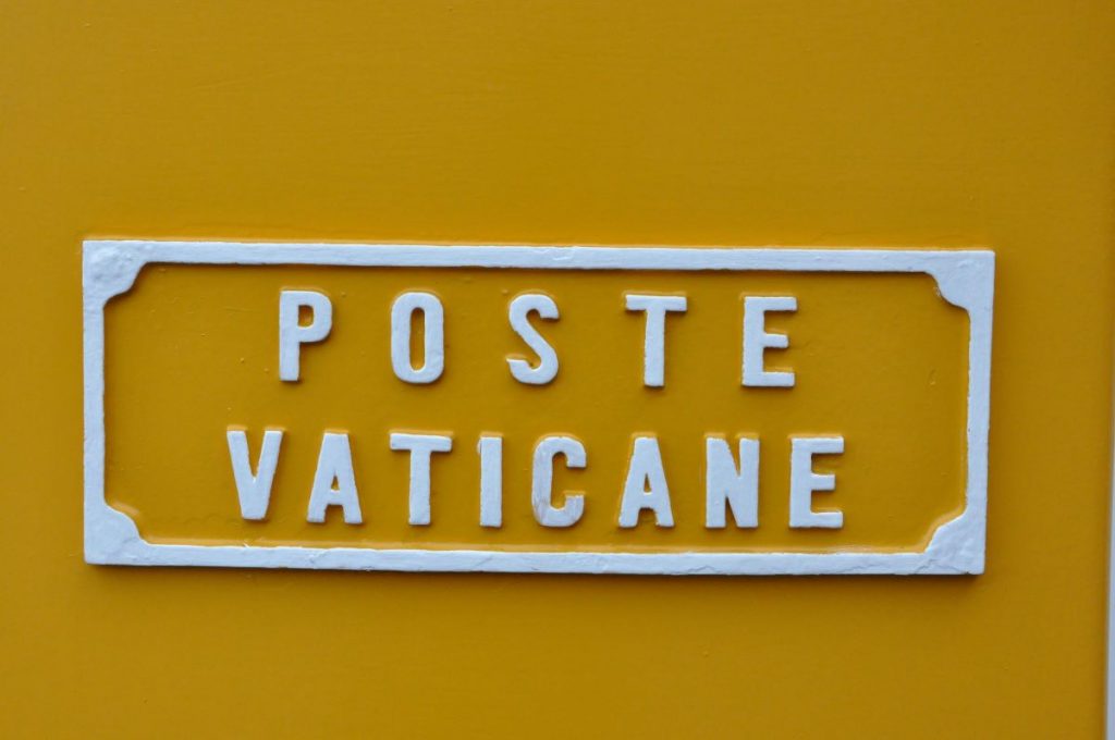 A yellow sign with white raised letters reads “POSTE VATICANE,” identifying the entrance to Vatican City’s famous post office.