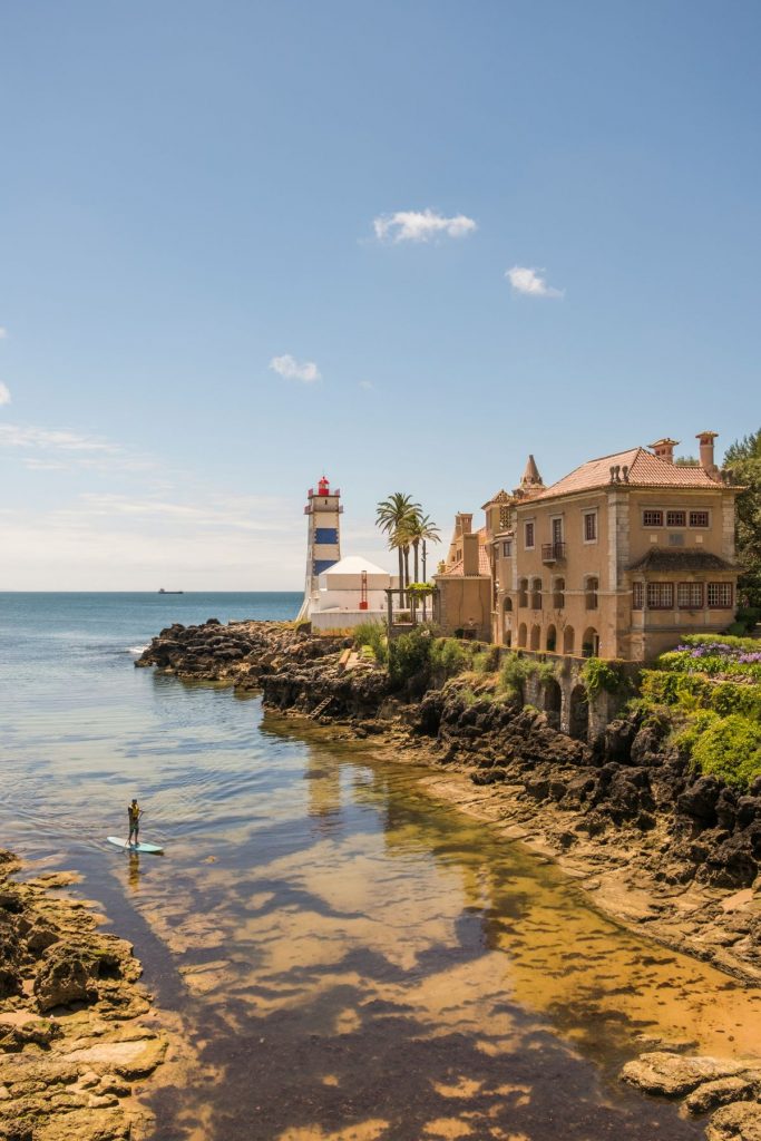 A man paddle boarding in Cascais near a lighthouse. One of the many day trips from Lisbon.