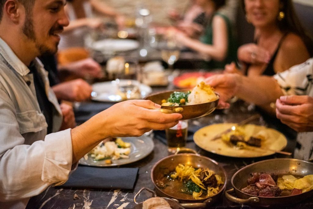 Several people sit around a restaurant table in Portugal, laughing and sharing seasonal Portuguese dishes made from fresh, local ingredients.