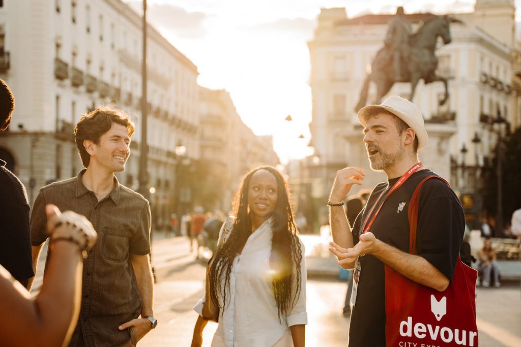 Three adults converse and laugh in Plaza del sol, Madrid, with historic buildings behind them.