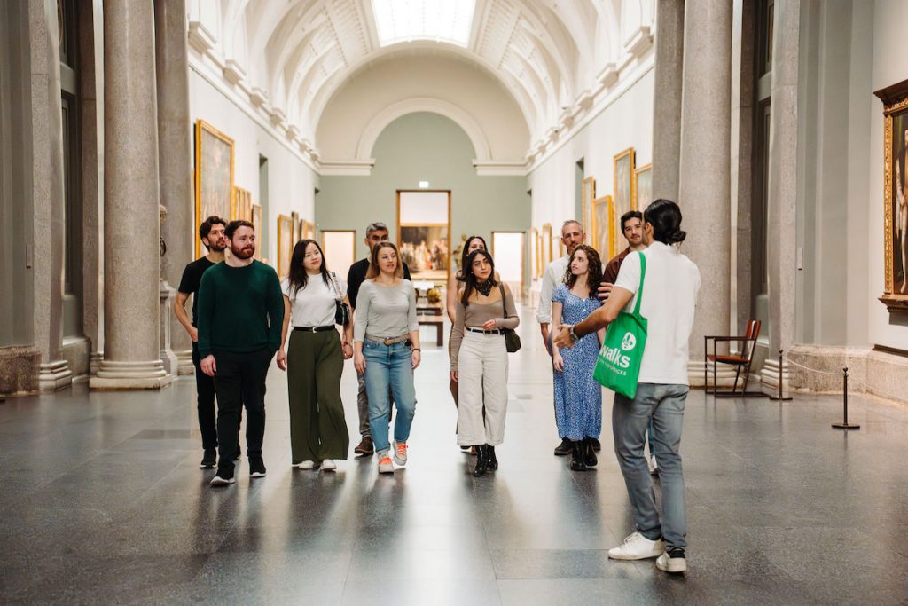 Group of tourist walking in the Prado Museum in Madrid. following a tour guide with a green tote bag.