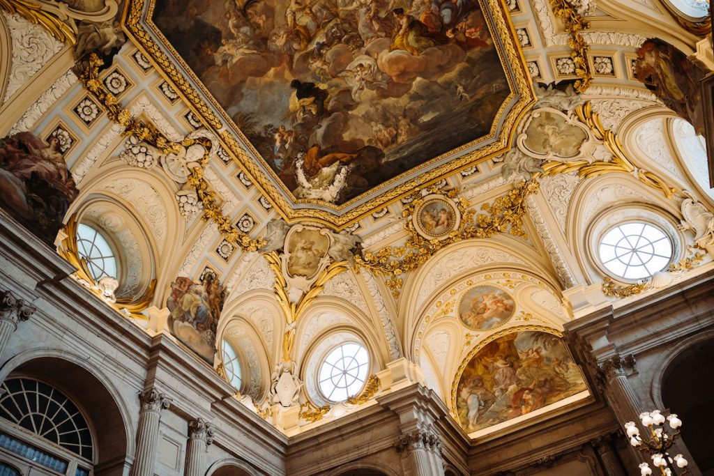 The lavish frescoed ceiling of Palacio Real in Madrid, Royal Palace glows with gold accents and arched windows.