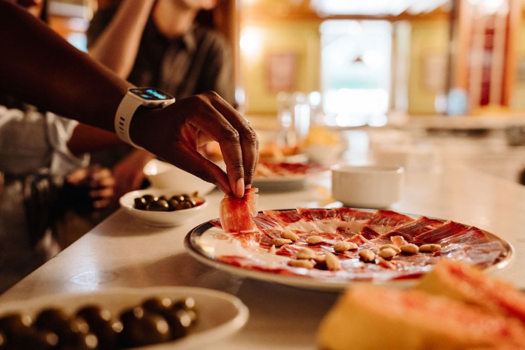 Hand taking some Spanish Ham from a tapas plate, with other dishes in the background