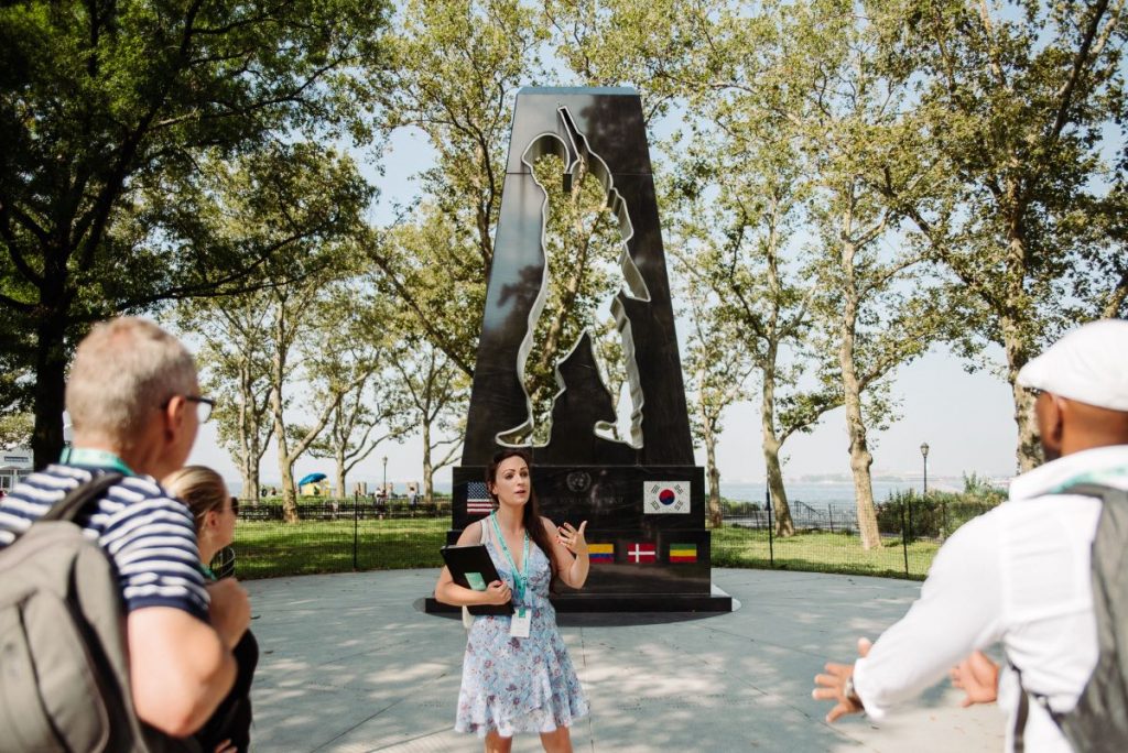 A group of people listening to a woman talking about the Korean War Veterans Memorial in NYC.