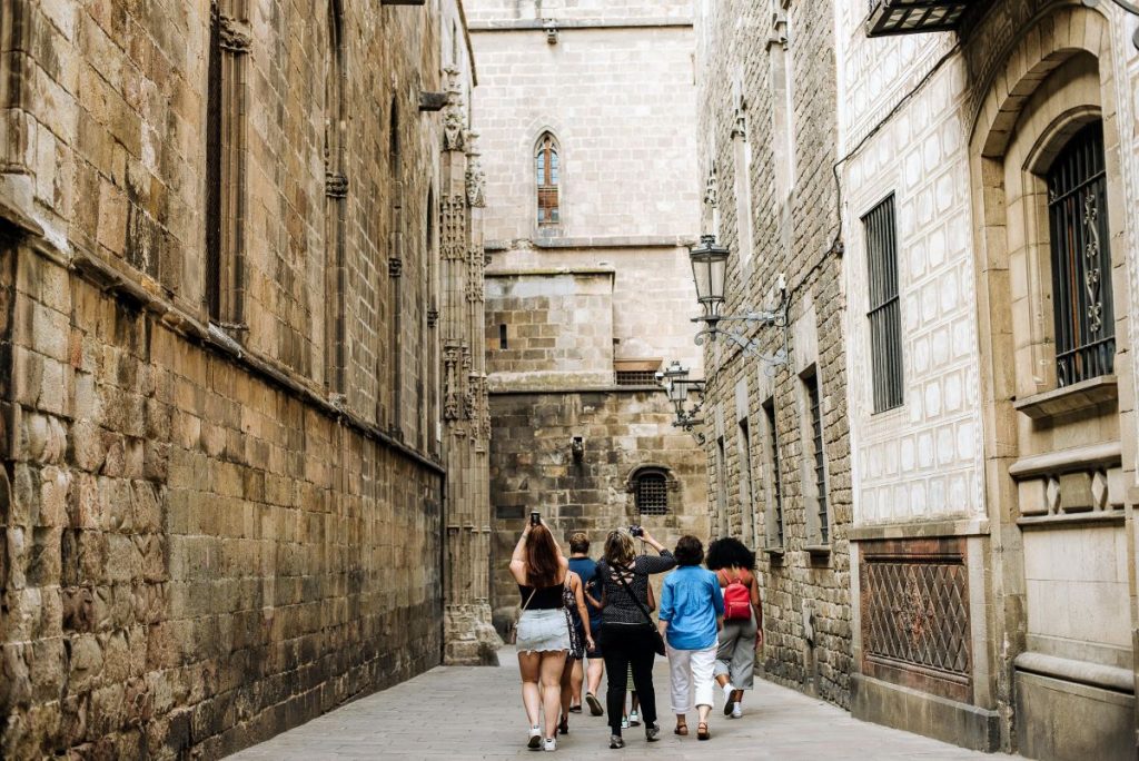People stroll down a narrow alley in Barcelonas Gothic Quarter, surrounded by historic stone buildings and old-fashioned lanterns.