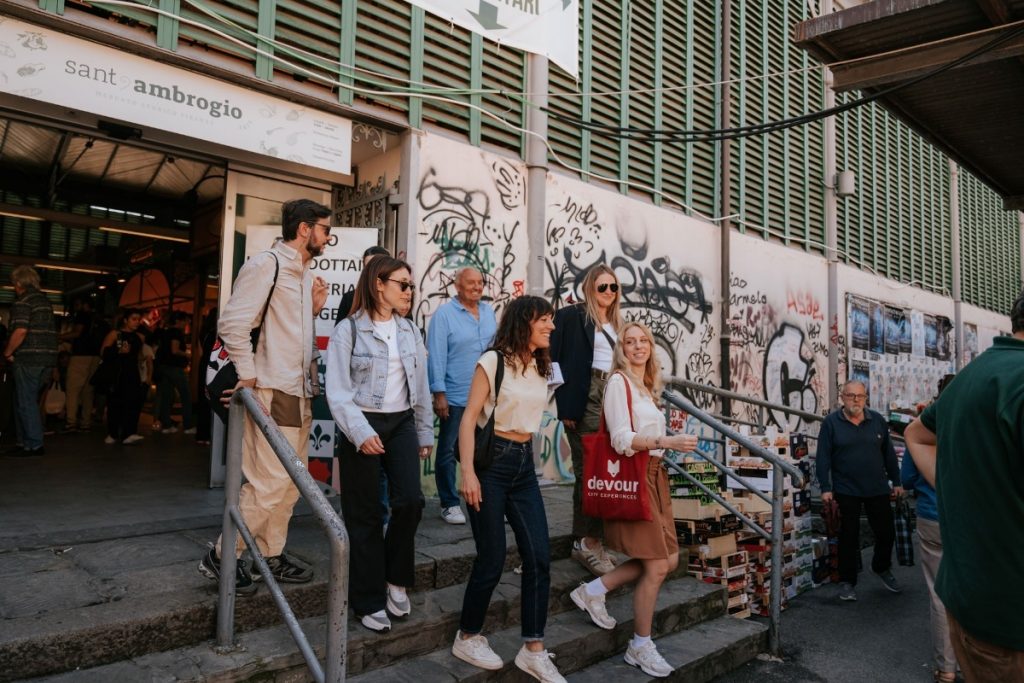 Several people descend steps outside Sant’Ambrogio, Florence; graffiti covers the walls beside them near the busy SantAmbrogio market.