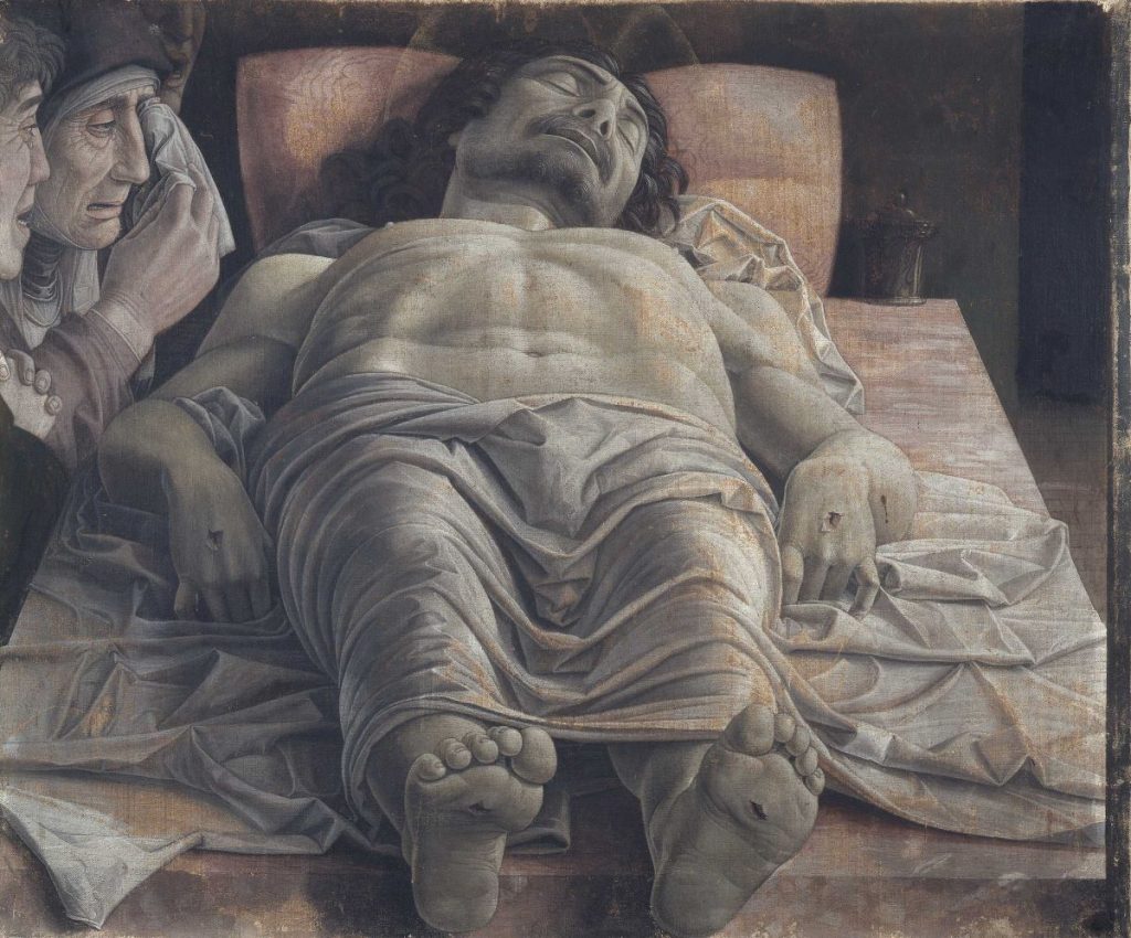 Christ’s body rests lifeless on a stone slab at the Pinacoteca di Brera in Milan, mourned by two grieving figures.