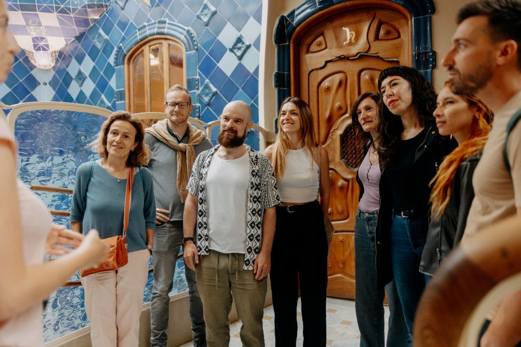 A cheerful group listens to a guide inside Lisbon’s Jerónimos Monastery, surrounded by blue azulejos and an ornate wooden door.