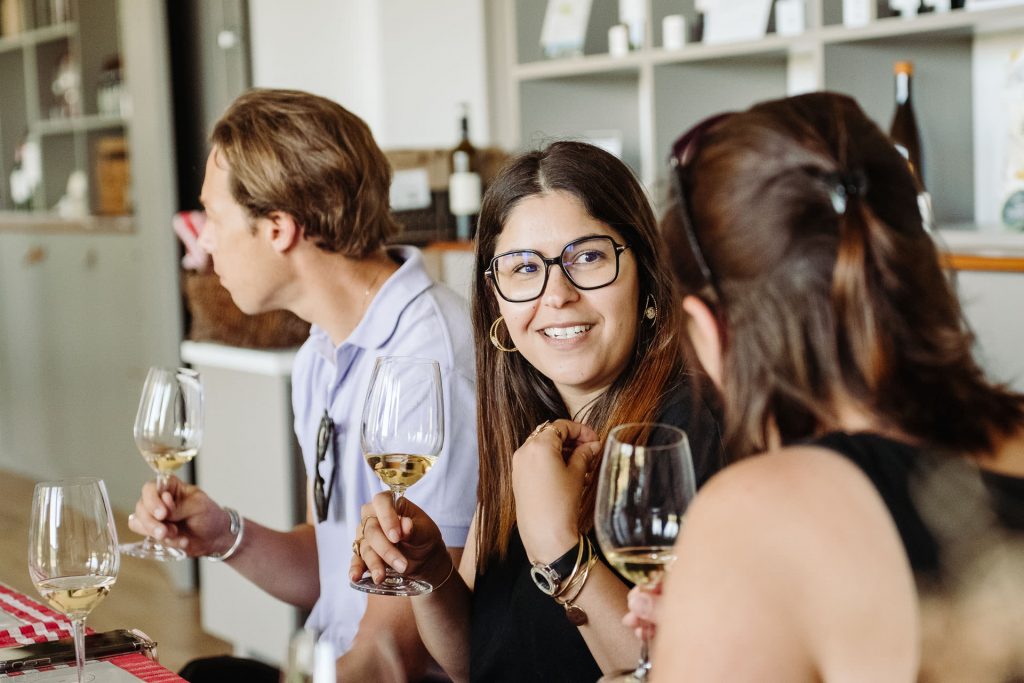 Three friends smile and toast with glasses of white wine at a cozy wine bar, discussing their favorite Bordeaux selections.