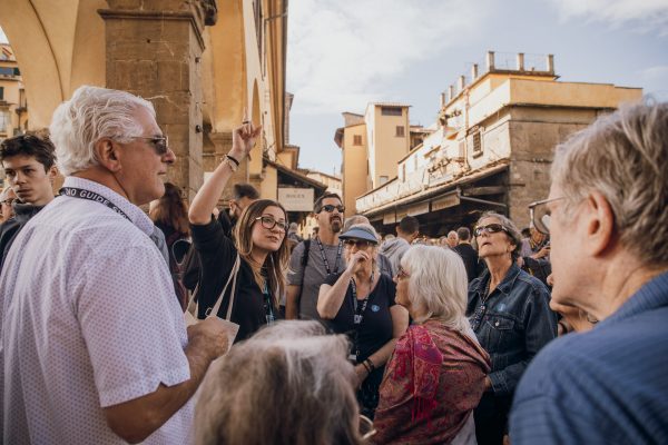 A tour guide gestures while explaining Florences Renaissance architecture to attentive tourists near historic arches on a sunny day.
