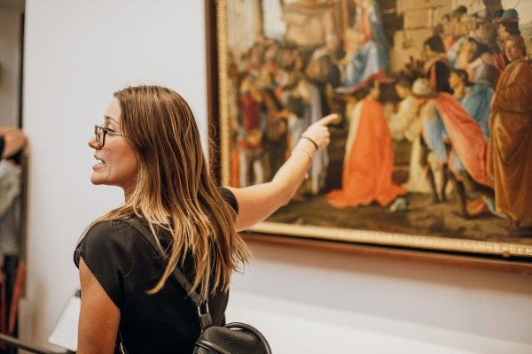 A woman with glasses and a black shirt gestures toward Botticelli’s The Birth of Venus in Florence’s Uffizi Gallery.