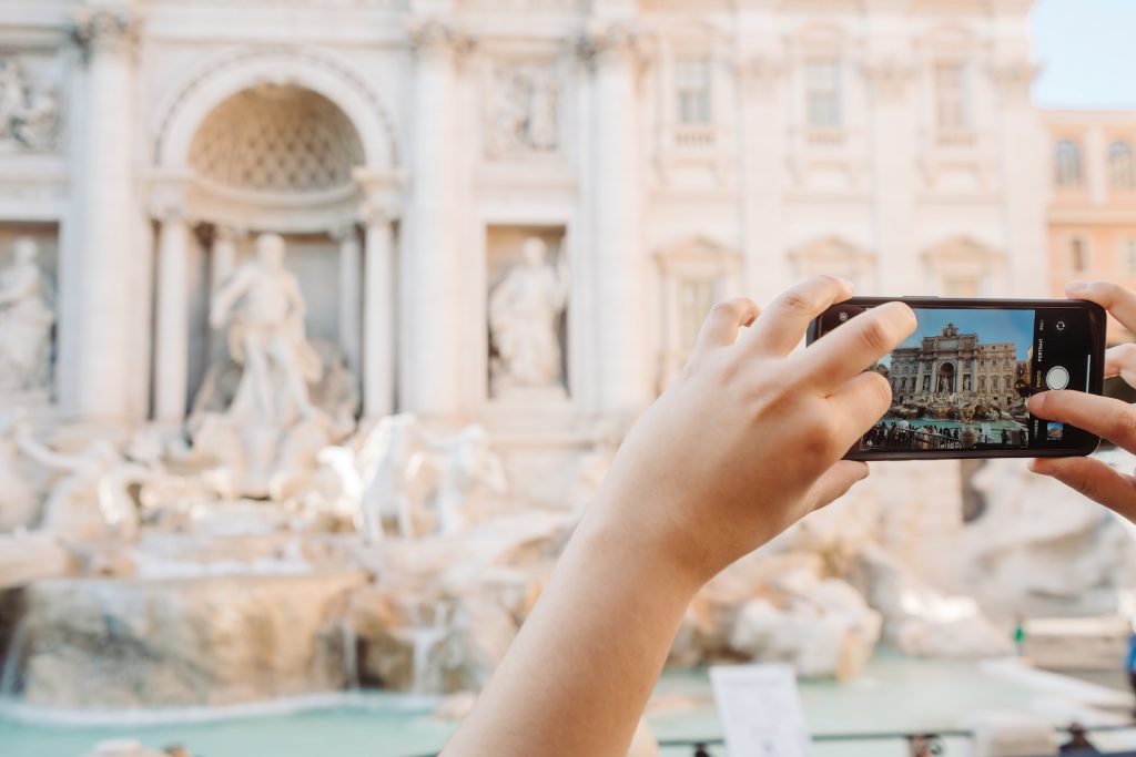 A person uses a smartphone to photograph Trevi Fountain in Rome, focusing on its ornate sculptures and cascading water.