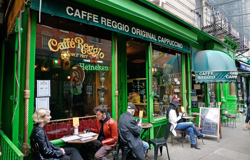 People sit at small outdoor tables at Caffe Reggio, a bright green café in New York’s lively Greenwich Village neighborhood.