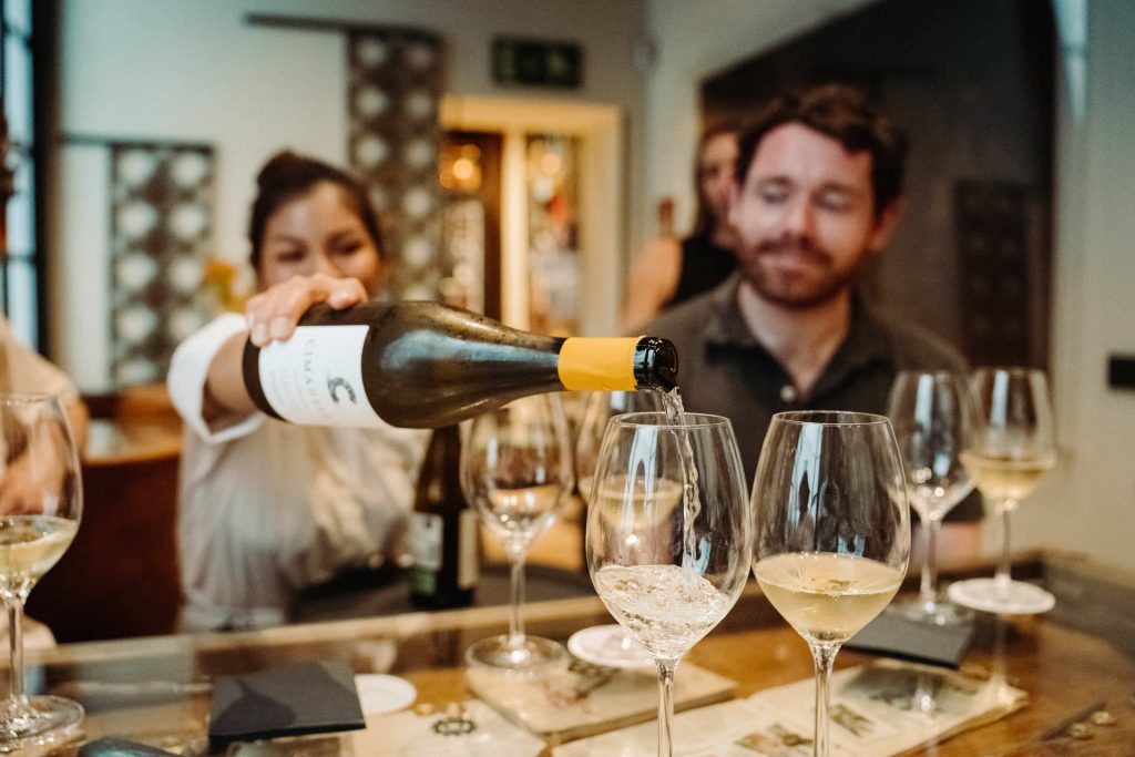 A woman pours white wine for smiling customers at a popular Naples bar, known as one of the city’s top eateries.