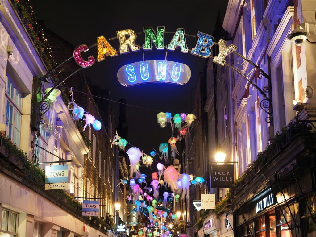Carnaby Street in Soho, London, lit up at night with colorful “Carnaby” sign and glowing jellyfish-shaped decorations overhead.