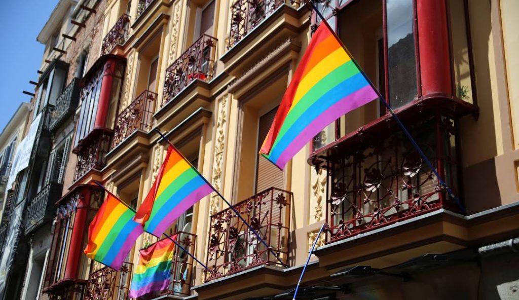 Rainbow pride flags displayed on the balconies of a historic building in Chueca, the Madrid gay district, symbolizing LGBTQ+ visibility and inclusion.