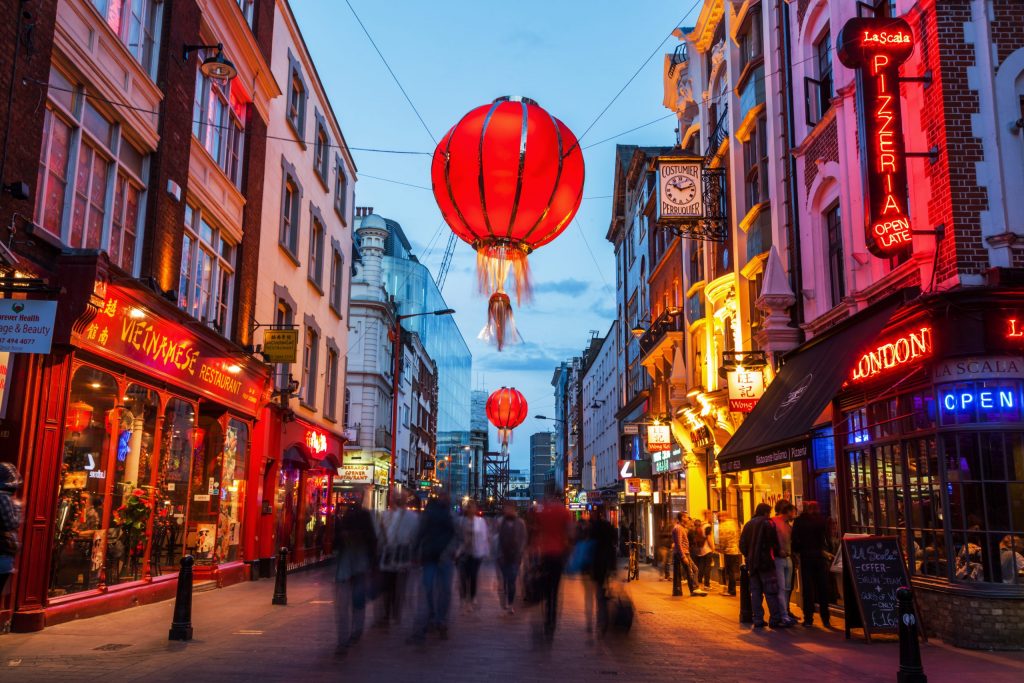 A lively evening in London’s Chinatown with red lanterns hanging above and neon-lit restaurants on both sides.