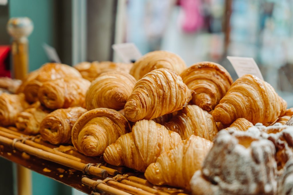 Freshly baked croissants are stacked on a wooden rack in a Paris bakery, with a sugared pastry placed in front.