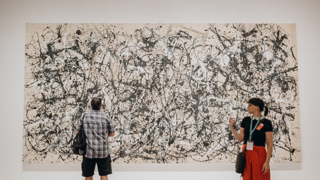Two people discuss Jackson Pollocks Number 32 with black, white, and beige splatters in a modern art gallery.