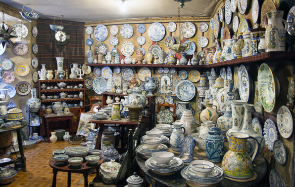 Shelves and tables in a shop overflow with vibrant ceramic bowls, vases, and plates; every surface holds travel-themed gifts.