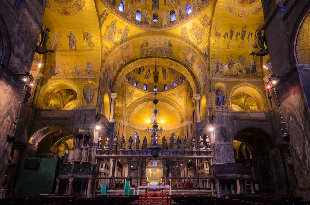 Visitors admire gold mosaics, statues, and religious paintings under high domes inside Saint Mark’s Basilica in Venice.