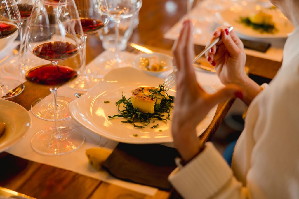 A person prepares to eat a round savory dish on greens at a wooden table in Rome, with red wine and water glasses nearby.