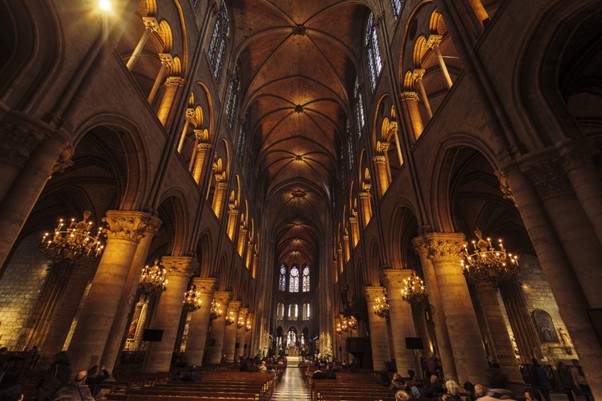 Visitors sit quietly in Sainte Chapelle, Paris, as soft candlelight glows among the soaring stone arches and pews.