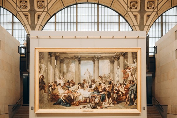 A classical painting at the Impressionist Museum in Paris shows people in Roman attire conversing among grand columns.