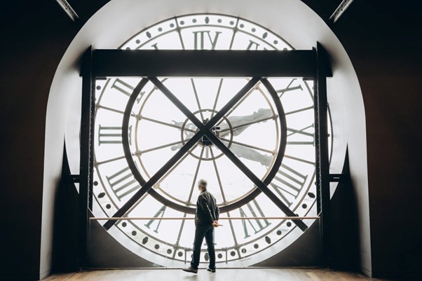 A person at Musée d'Orsay in Paris stands silhouetted against the large clock, looking out as sunlight floods through.