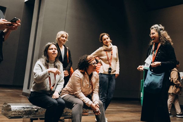 Five women at the Musee d´Orsay talk together, wearing lanyards. One woman holds a brochure.